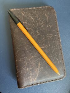 Leather notebook cover with a yellow Bic pen on top against a blue background