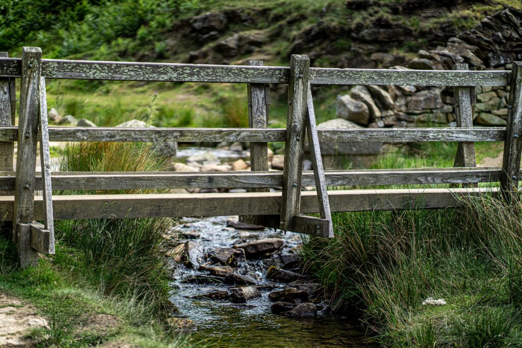 Public domain image of a small wooden bridge that crosses a stream between two close banks.
