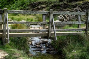 Public domain image of a small wooden bridge that crosses a stream between two close banks.